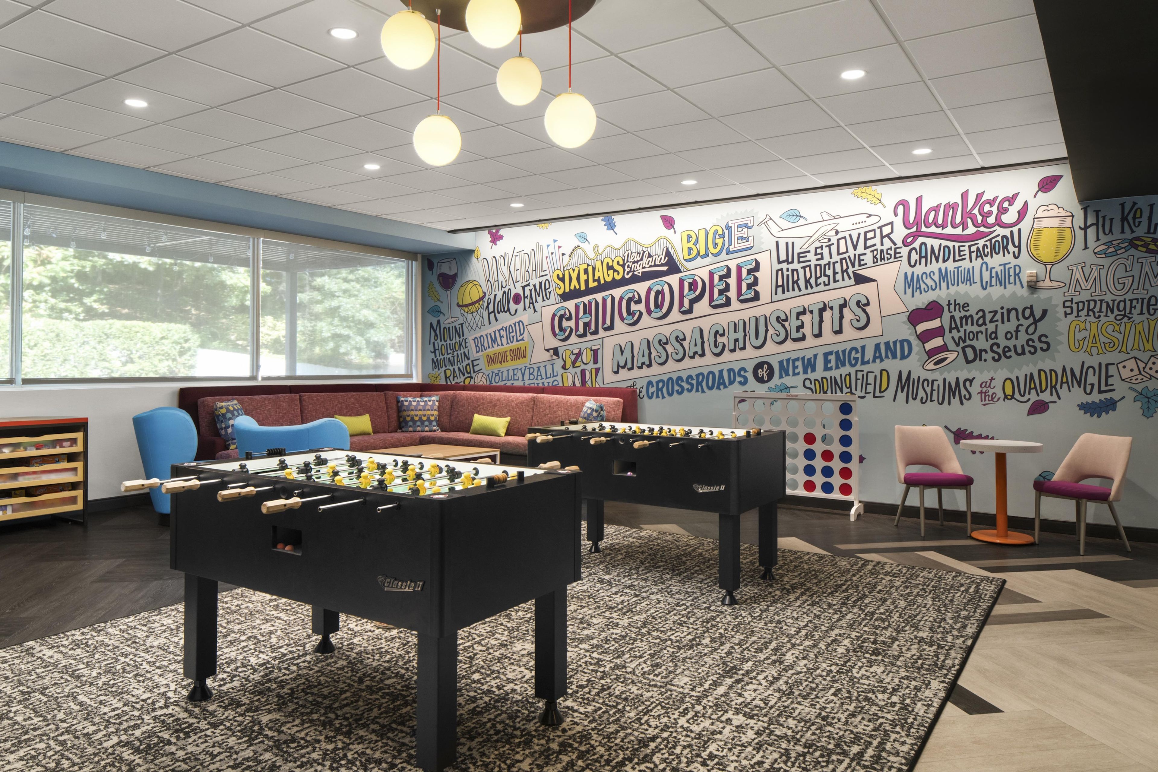 A room with a foosball table, a sofa, and a wall with various attractions listed.