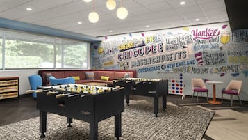 A room with a foosball table, a sofa, and a wall with various attractions listed.