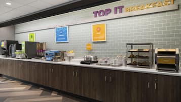 A breakfast buffet area with a sign reading 'TOP IT BREAKFAST' and various food items displayed.