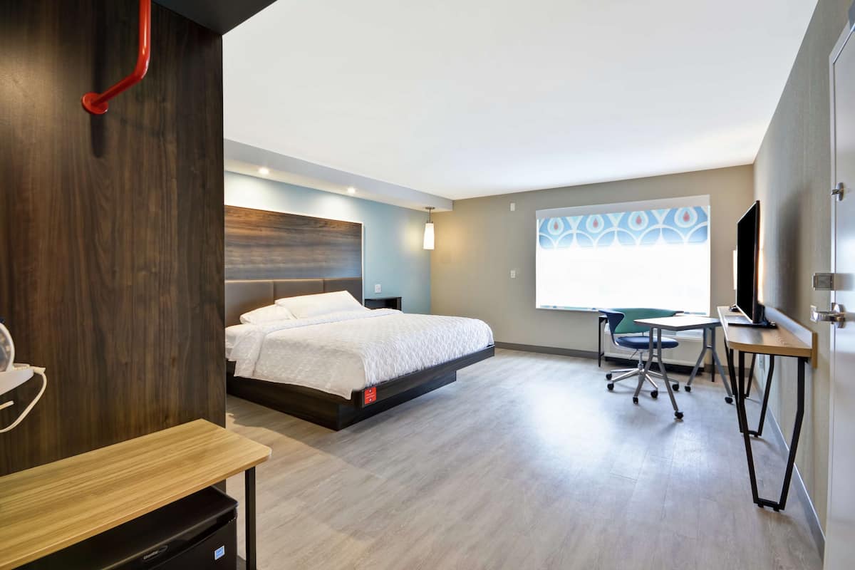 Una habitación de hotel moderna con cama, escritorio, silla y un ventanal con vistas.