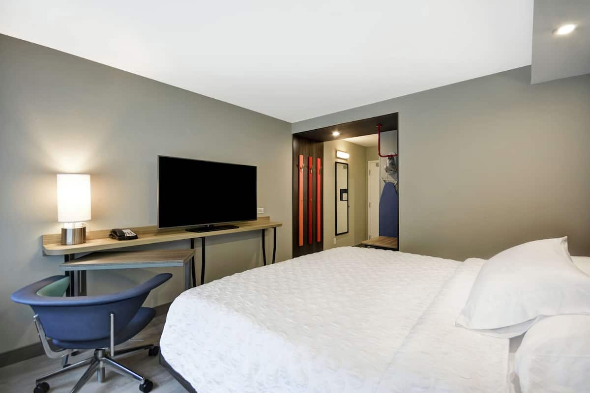Una habitación de hotel con una cama, un escritorio con televisor, una silla y un espejo.