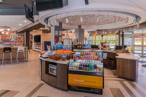 A modern cafe with a central counter, seating area, and a display of beverages. - Tru by Hilton Little Rock West (Little Rock)