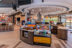 Una cafetería moderna con un mostrador central, zona de estar y una exhibición de bebidas.