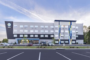 Un hôtel moderne doté d’un toit plat, de nombreuses fenêtres et d’un parking où sont stationnées plusieurs voitures.