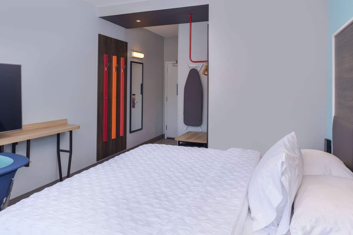 A modern hotel room with a large bed, a desk, and a mirror.