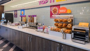 Una barra de desayuno con un letrero que dice "TOP IT BREAKFAST", que ofrece bagels, rosquillas y cereales.