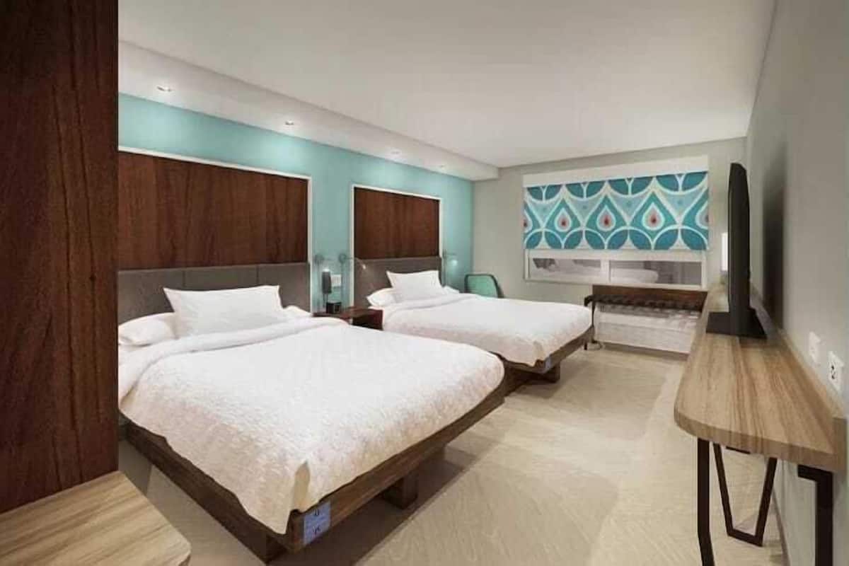 A modern hotel room with two beds, a wooden desk, and a large window.