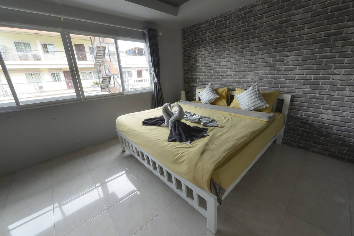 A bedroom with a bed, a brick wall, and a window with curtains.
