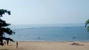 Uma praia com céu claro, mar calmo e algumas pessoas.