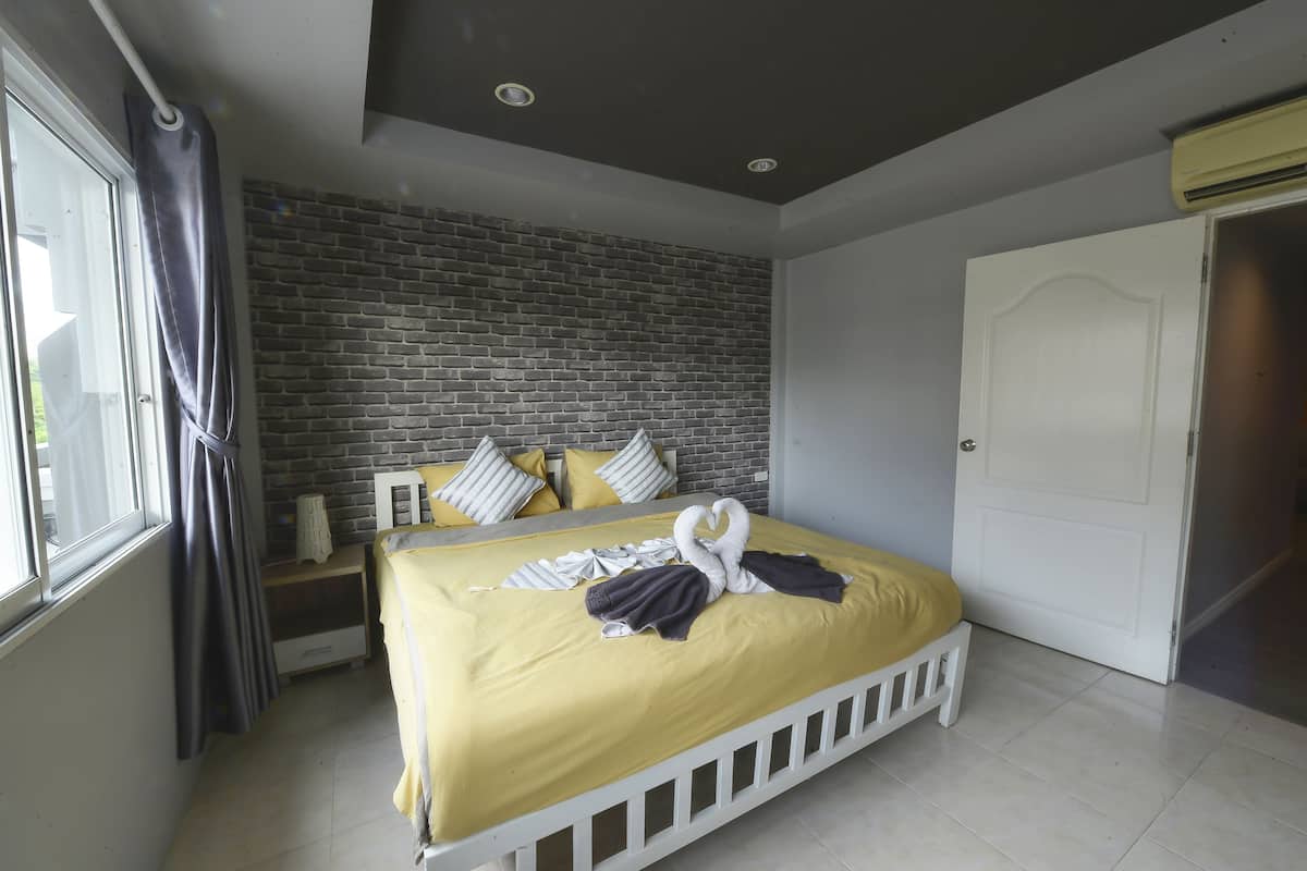 A hotel room with a brick-patterned wall, a white door, and a bed with a yellow bedspread and white headboard.