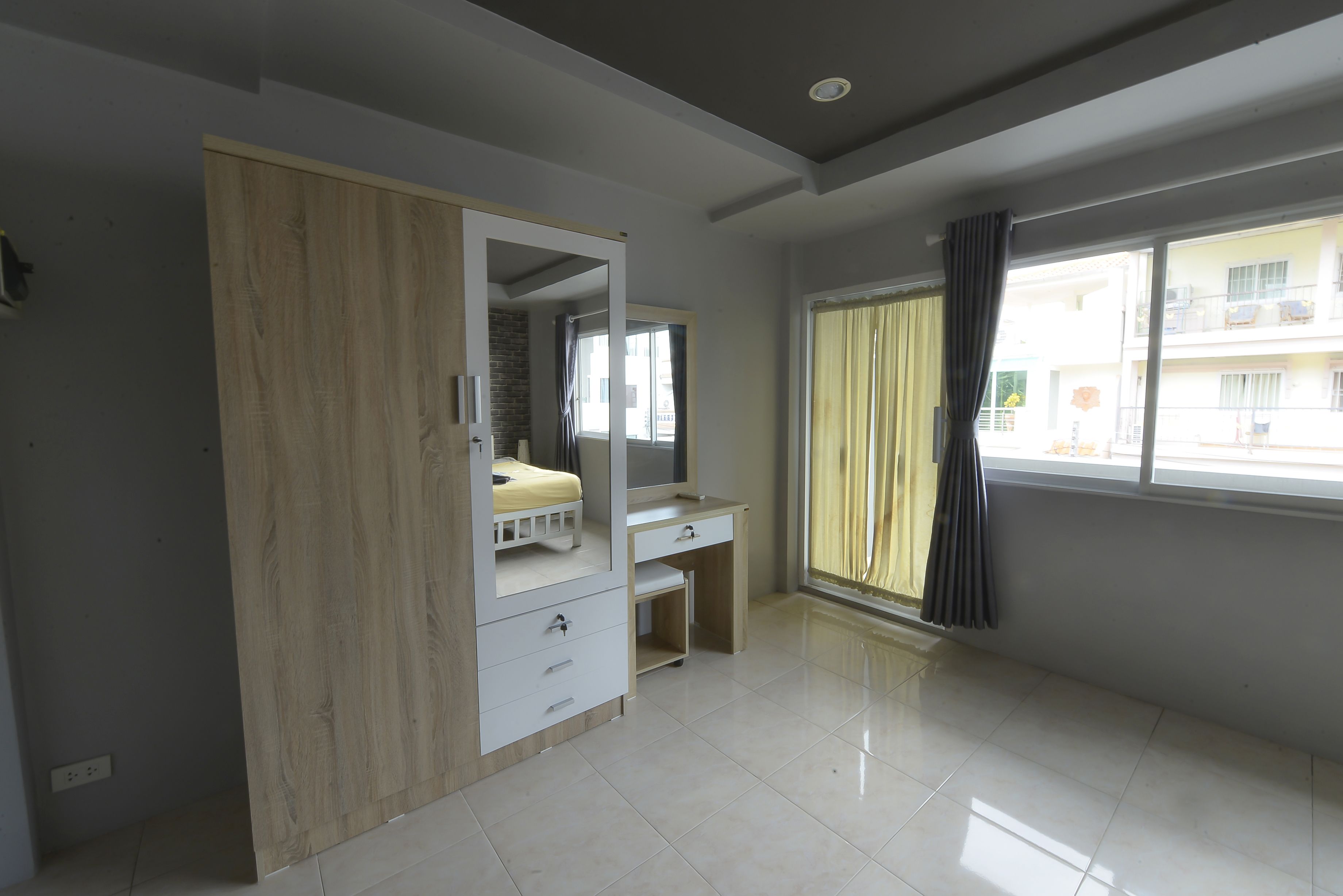 A room with a wardrobe, a desk, and a window with curtains.