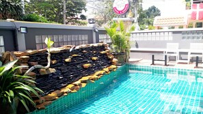 A swimming pool with a rock-lined edge and a small waterfall feature. - Livit70's hotel & hostel (Pattaya)