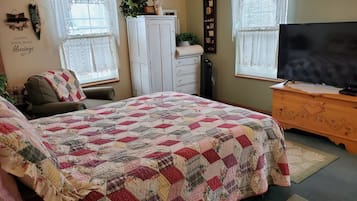 A bedroom with a large bed, a chair, a dresser, a television, and two windows with curtains.