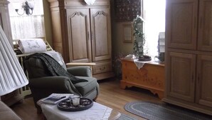 A cozy living room with a sofa, a coffee table with magazines, a lamp, and a large wooden cabinet. - Alaska's Lake Lucille B&B (Wasilla)