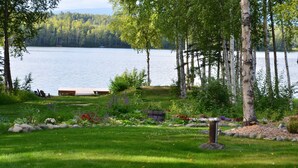 A lakeside garden with a wooden deck, a stone pathway, and a variety of plants and flowers. - Alaska's Lake Lucille B&B (Wasilla)