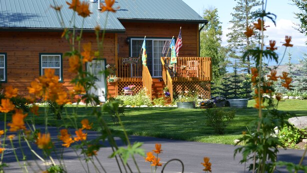 A wooden cabin with a metal roof, surrounded by a well-maintained garden and a clear view of the mountains. - Alaska's Lake Lucille B&B (Wasilla)