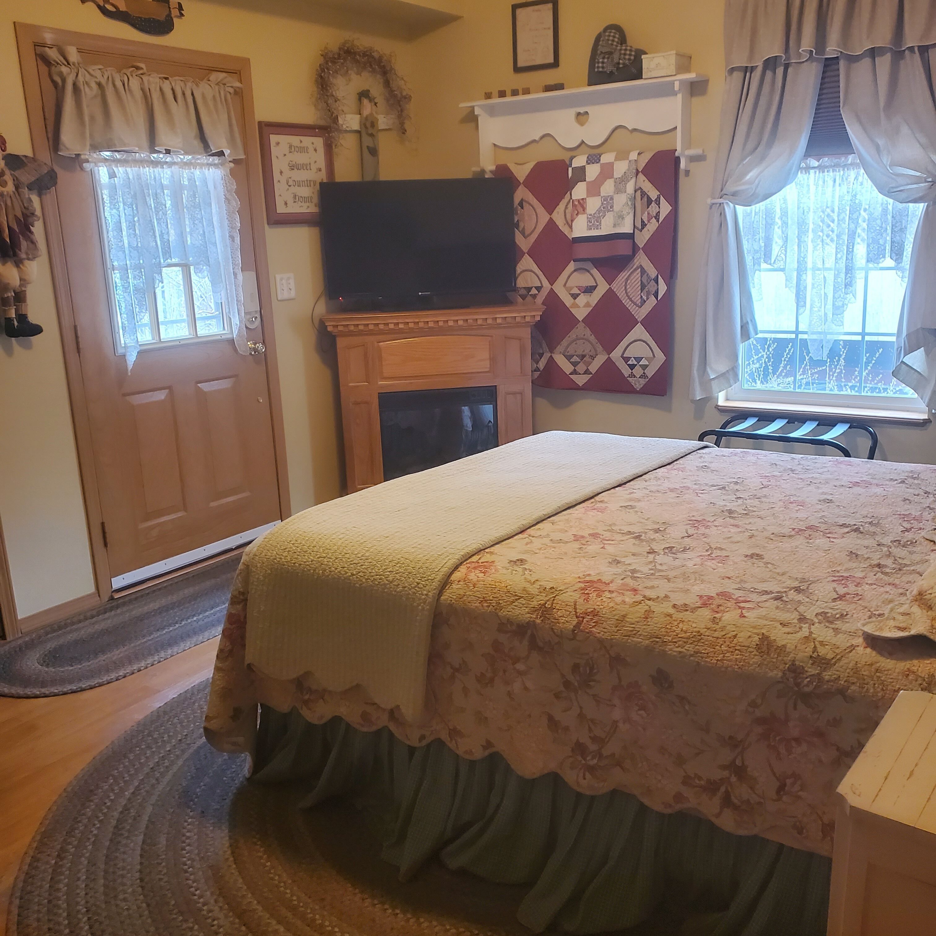 A bedroom with a bed, a television, a fireplace, and a window with curtains.