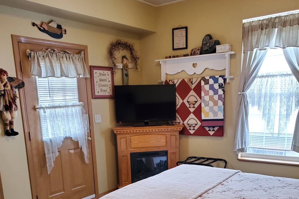 A bedroom with a bed, a television on a stand, a fireplace, and a window with curtains.