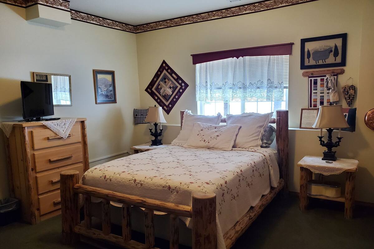 A bedroom with a wooden bed, a dresser, a television on top, and a window with curtains.