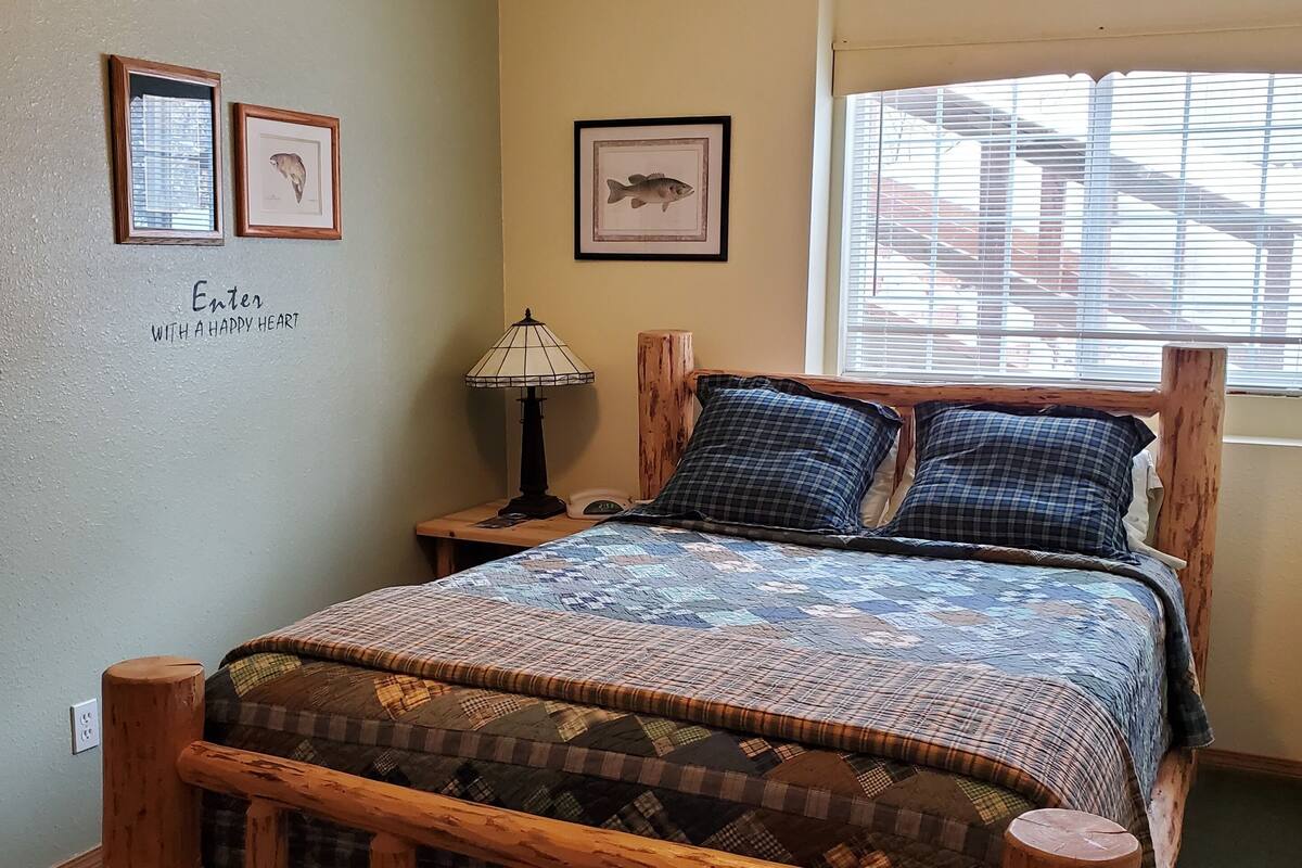 A bedroom with a wooden bed frame, a quilt, a bedside lamp, framed fish pictures, and a 'Welcome' sign.