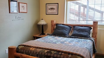 Un dormitorio con estructura de cama de madera, colcha, lámpara de noche, cuadros enmarcados con imágenes de peces y un letrero que dice 'Welcome'.