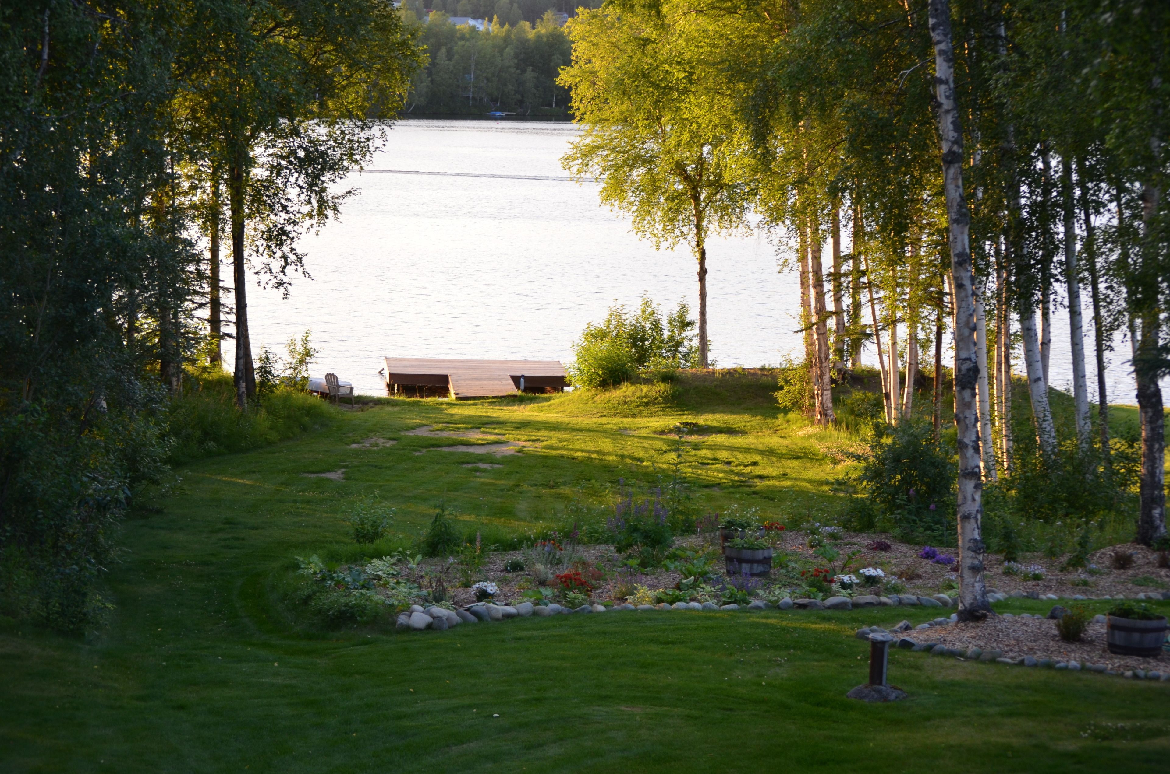 A serene lakeside property with a wooden deck, lush greenery, and a clear view of the water.