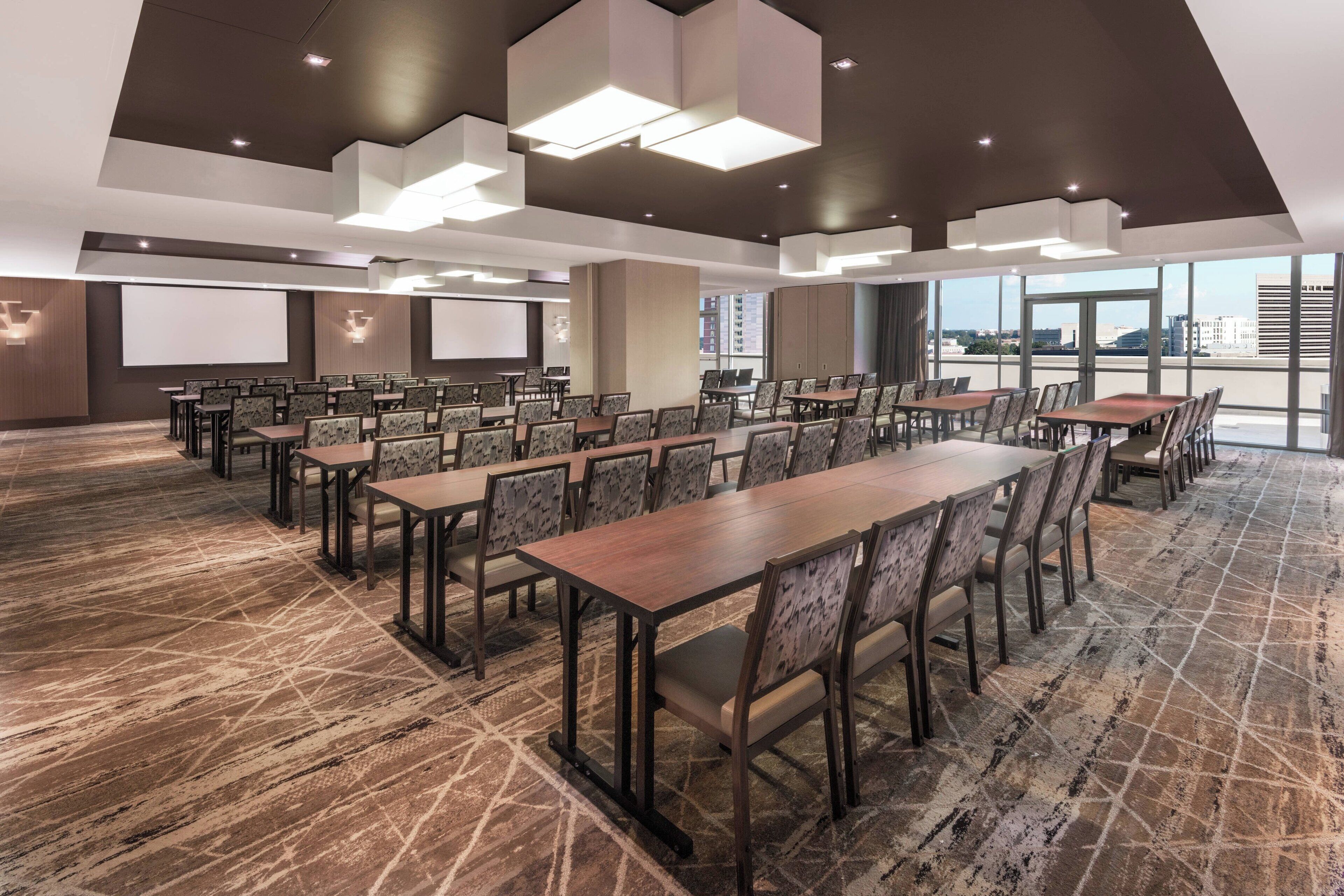 A conference room with multiple tables and chairs, a large screen, and a carpeted floor.