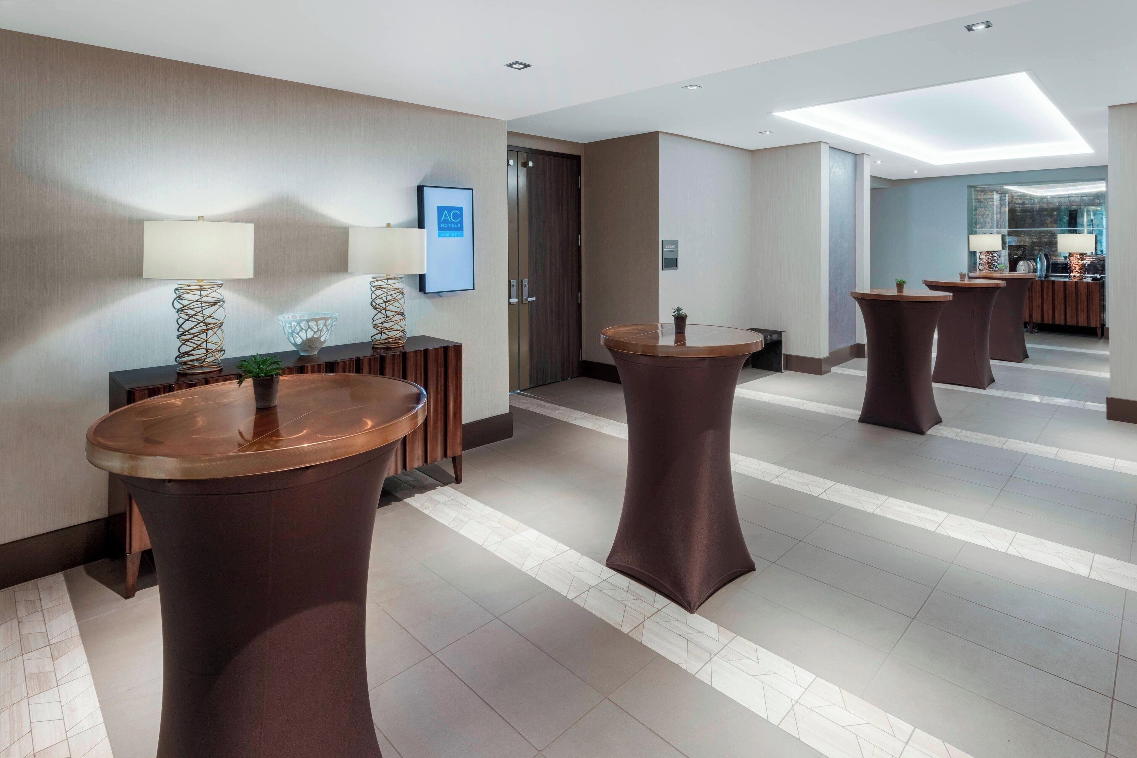 A hotel lobby with round tables, a reception desk, and a modern interior design.