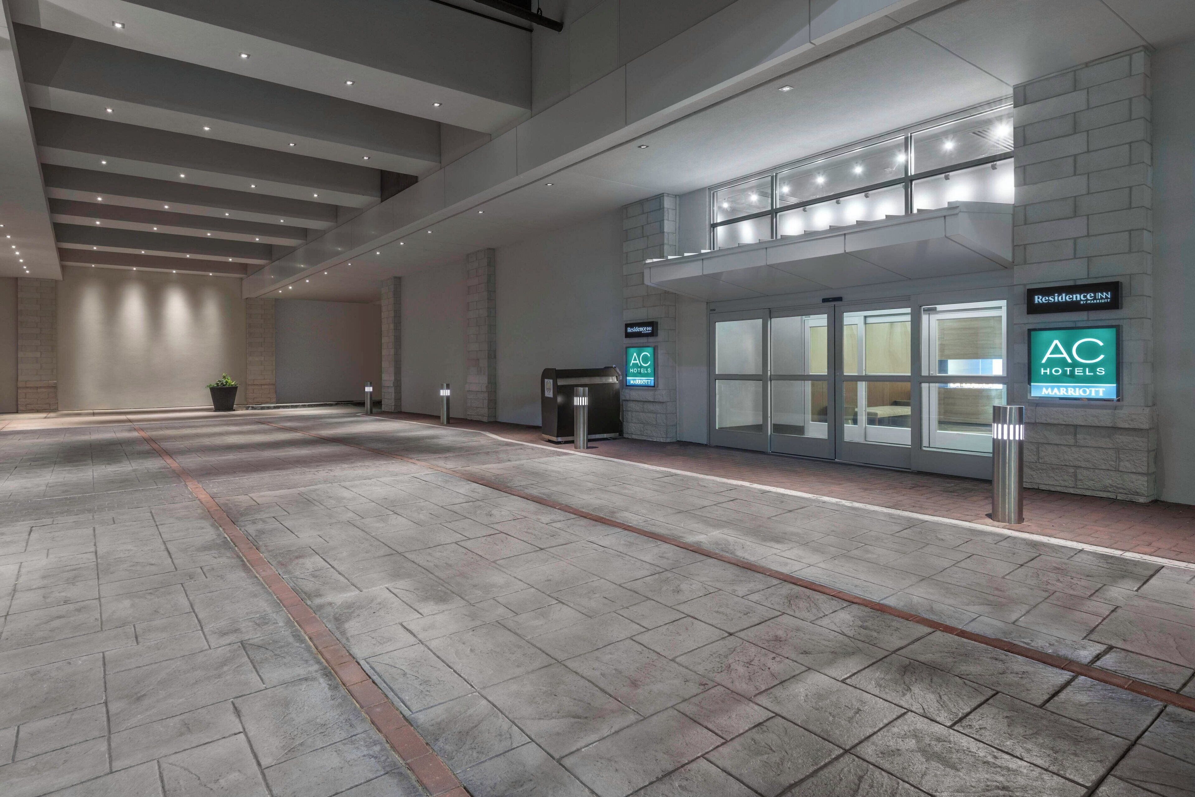 A spacious lobby with a modern design, featuring a reception desk, a coffee machine, and signage for AC Hotels and Marriott.