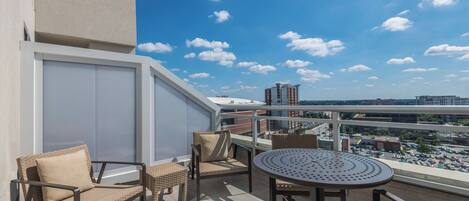 A balcony with wicker furniture, a round table, and a view of the cityscape.