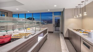 A modern hotel room with a breakfast buffet, large windows with a city view, and contemporary lighting fixtures. - AC Hotels by Marriott Charlotte City Center (Charlotte)