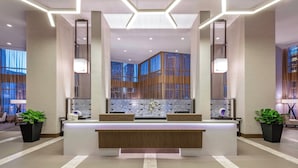A modern hotel lobby with a reception desk, large windows, and a geometric ceiling design. - AC Hotels by Marriott Charlotte City Center (Charlotte)