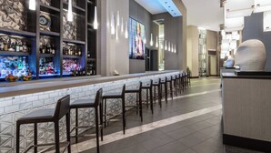 A bar area with a long counter, multiple bar stools, and shelves stocked with bottles. - AC Hotels by Marriott Charlotte City Center (Charlotte)