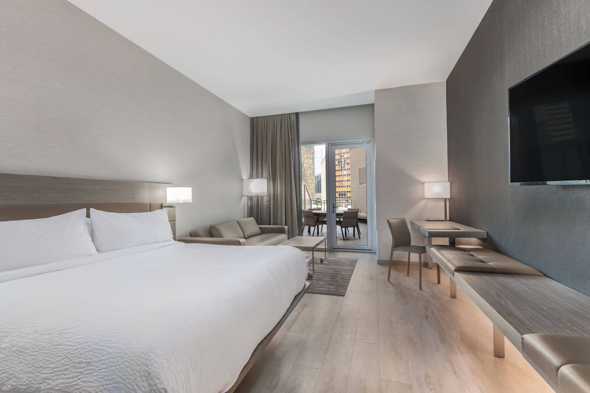 A modern hotel room with a large bed, a desk, a sofa, and a TV.