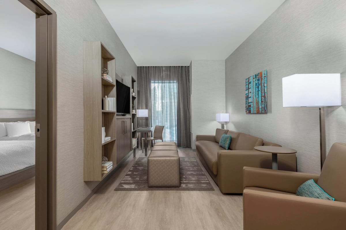 A modern hotel room with a bed, a sofa, a small table, a TV, and a desk with a chair.