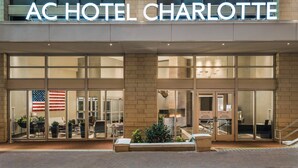 The exterior of AC Hotel Charlotte with large glass doors, a visible American flag, and a brick facade. - AC Hotels by Marriott Charlotte City Center (Charlotte)