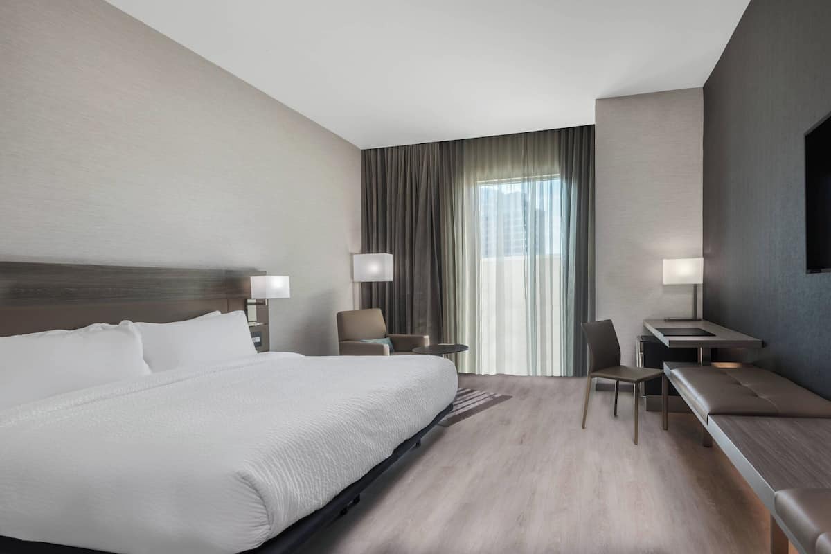 A modern hotel room with a large bed, a desk, a chair, and a sofa.
