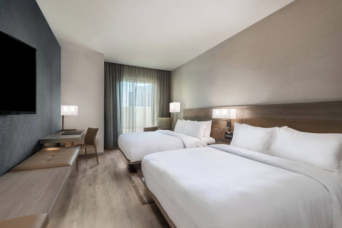 A hotel room with two beds, a desk, a chair, and a TV.