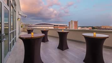 Eine Dachterrasse mit vier runden Tischen, jeder Tisch mit einer Kerze, mit Blick auf eine Stadtlandschaft mit modernen Gebäuden.