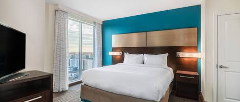 A hotel room with a large bed, a TV, a nightstand, and a view of the city through the window.