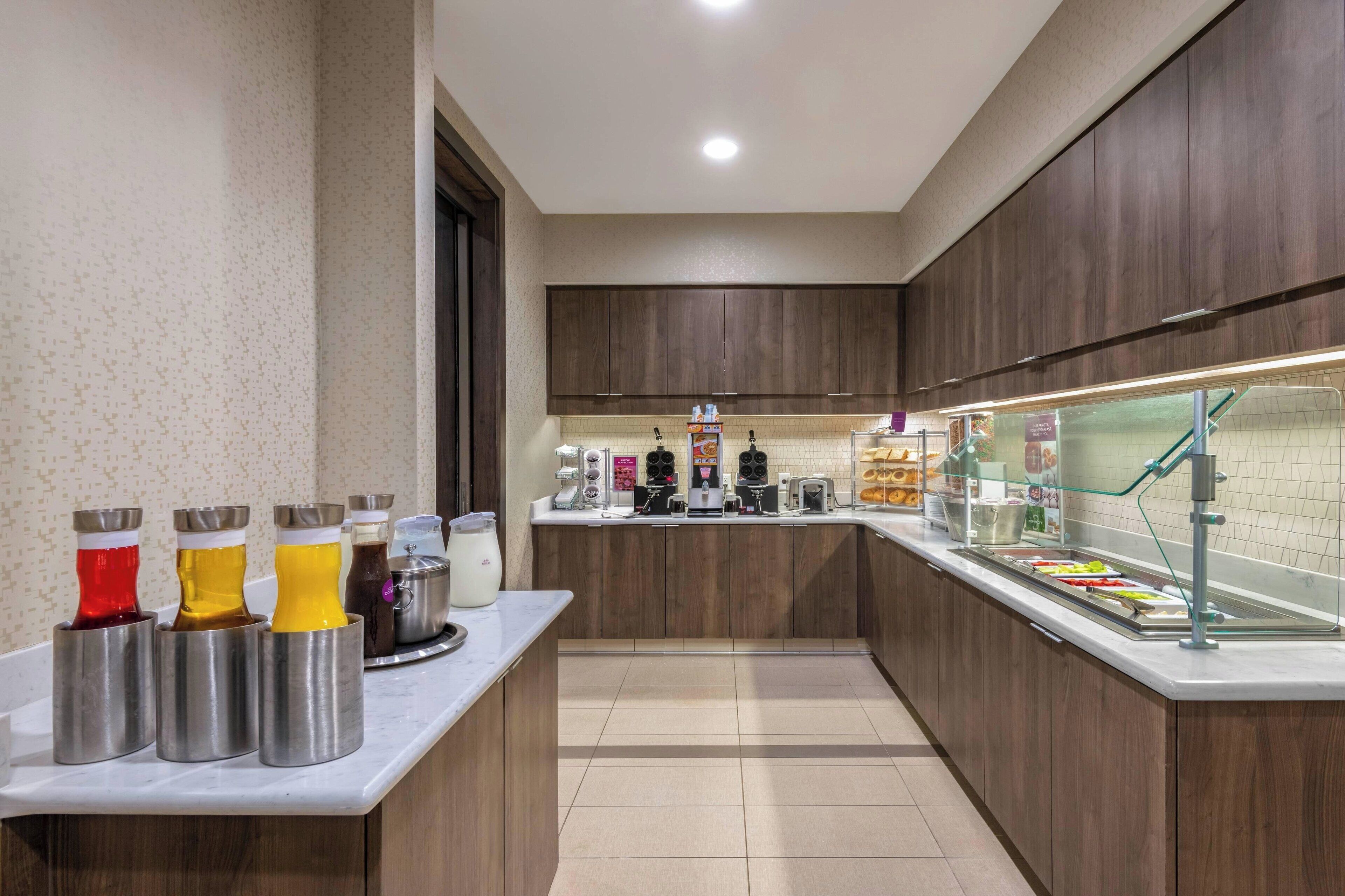 A modern kitchen with a marble countertop, stainless steel drink dispensers, a coffee station, and a glass display case.