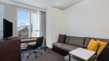 Une chambre d’hôtel moderne dotée d’une grande fenêtre, d’un canapé, d’une petite table et d’un bureau avec un téléviseur.