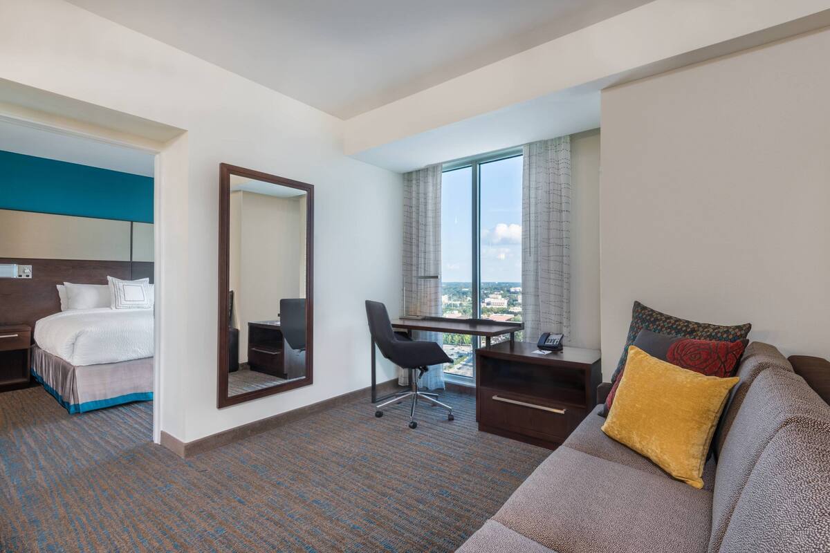 A hotel room with a bed, a desk, a chair, a sofa, and a large window with a view.