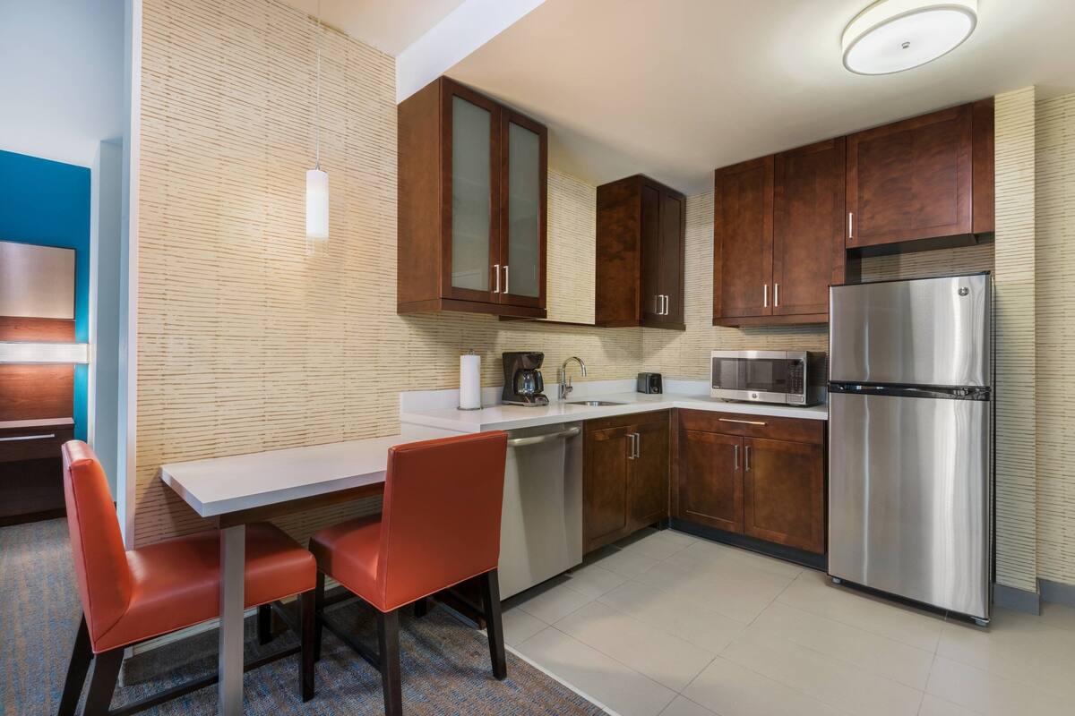 A modern kitchen with wooden cabinets, stainless steel appliances, and a dining area with red chairs.