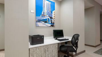 A modern office space with a white desk, a computer, a printer, and a chair. A large painting of a cityscape is on the wall.