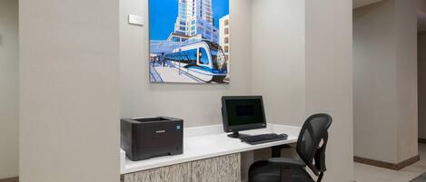 Un espacio de oficina moderno con un escritorio blanco, una computadora, una impresora y una silla. Un cuadro grande de un paisaje urbano adorna la pared.
