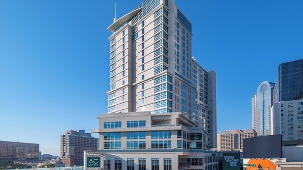 Un hôtel de grande hauteur, avec de nombreux étages, de grandes fenêtres et un logo de la marque AC bien visible.