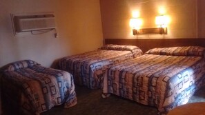 A hotel room with two single beds and a double bed, air conditioning unit on the wall, and two wall-mounted lights.