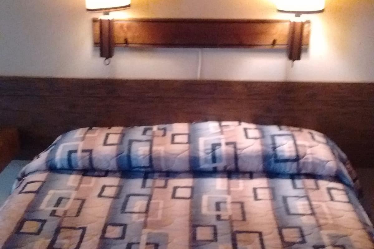 En säng med ett mönstrat överkast, två vägglampor och en inramad tavla på väggen.