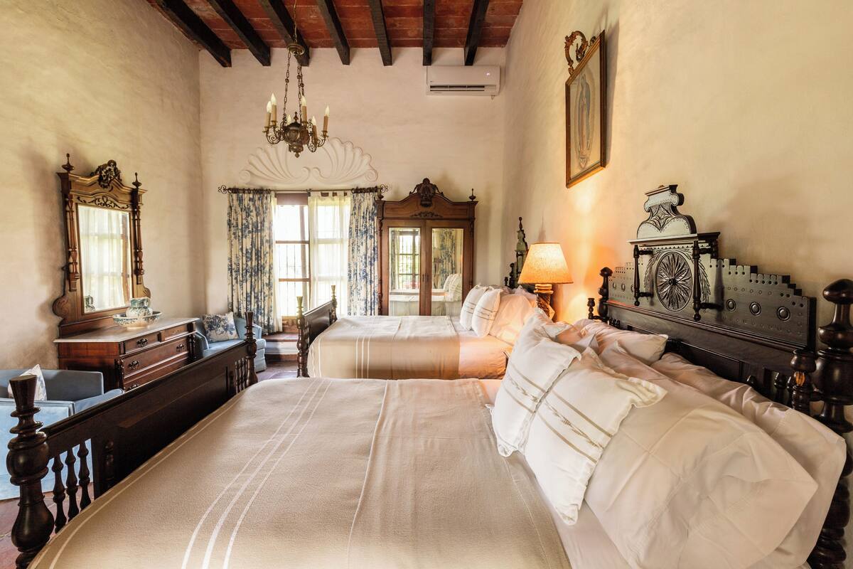 Quarto com duas camas, uma cômoda, um espelho e um candelabro.